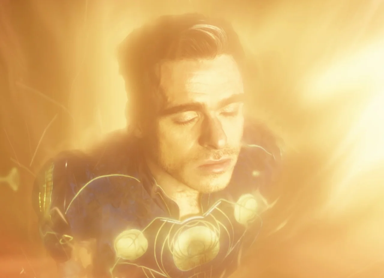 Eternals (2021) movie still: closeup — A man floats in deep space engulfed by intense, bright golden solar energy. The man keeps his eyes closed…