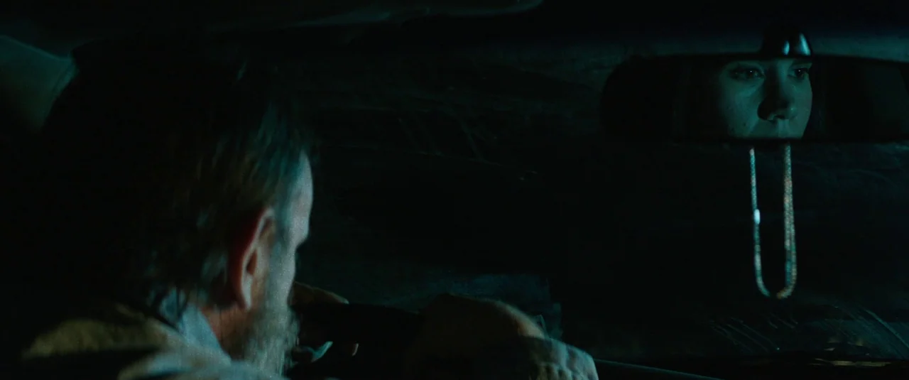 Southbound (2015) movie still: medium — The interior of a vehicle at night is engulfed in darkness. A man operates the steering wheel while a woman…