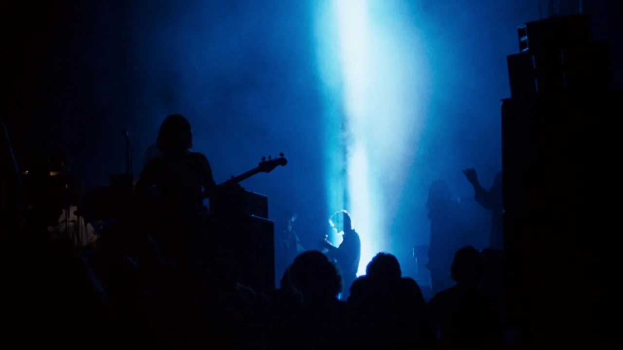 A Star Is Born (1976) movie still: wide — A darkened interior performance space filled with haze and saturated blue light. Multiple figures stand in…