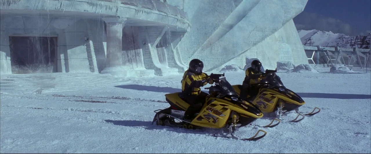 Die Another Day (2002) movie still: wide — A vast, flat snowy expanse lies before a massive, sculpted white ice building. Two riders on yellow…