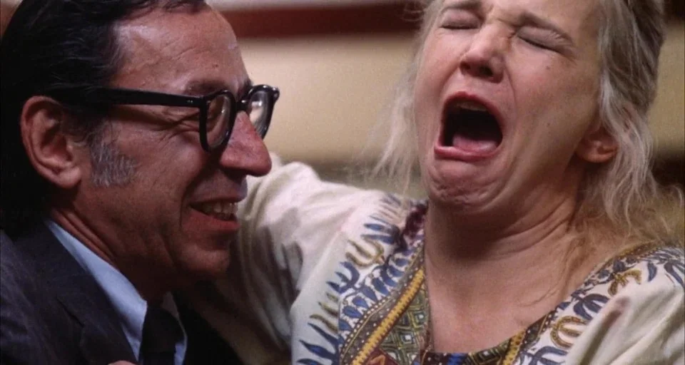 A Woman Under the Influence (1974) movie still: closeup — Two older adults occupy a brightly lit interior space. A man smiles while a woman beside…