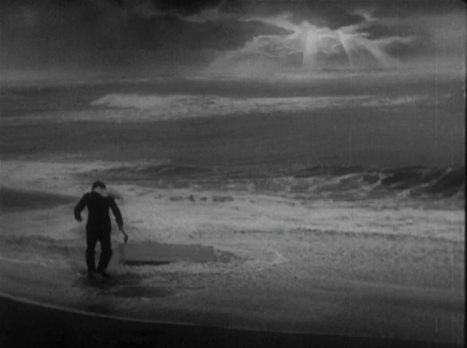Drunken Angel (1948) movie still: wide — A dark, stormy beach at night with heavy surf and a glowing cloud formation. A man in a suit drags a large…