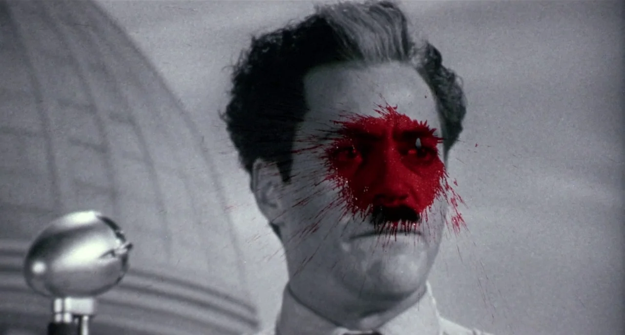 Chaplin (1992) movie still: closeup — A man stands before a microphone with a dome-shaped architectural element in the background. Bright red paint…