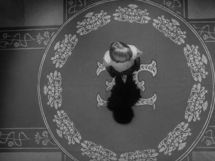 The Silence (1963) movie still: fullbody — A long hallway features a decorative rug with an intricate floral border pattern. A young boy stands at…