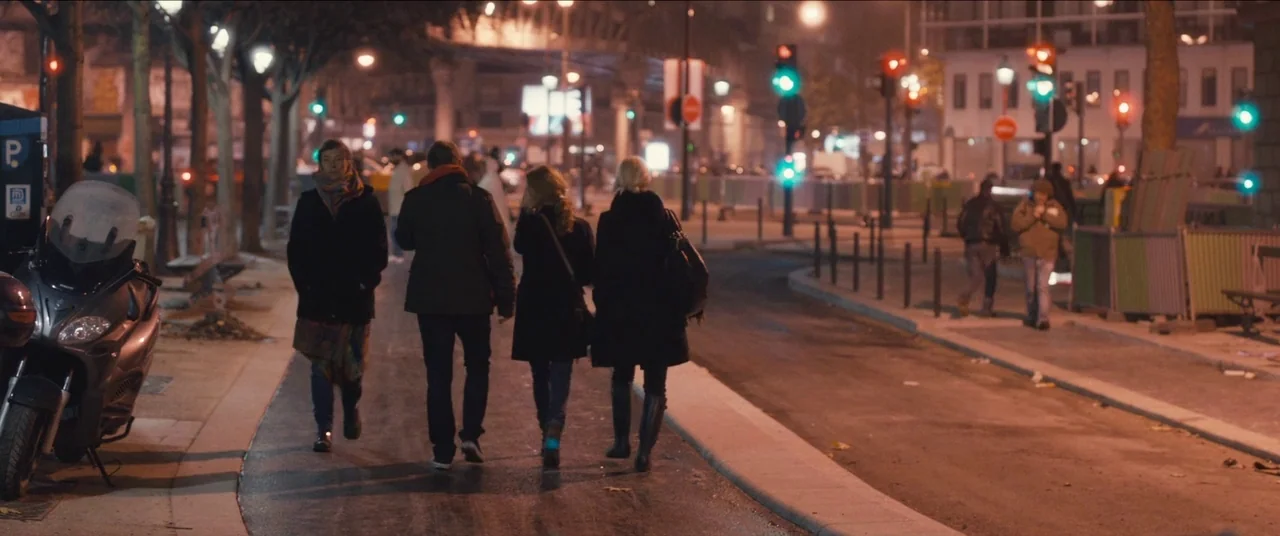 Simon Killer movie still: wide — A city street at night features traffic signals glowing green and red above pavement. Four people walk together…
