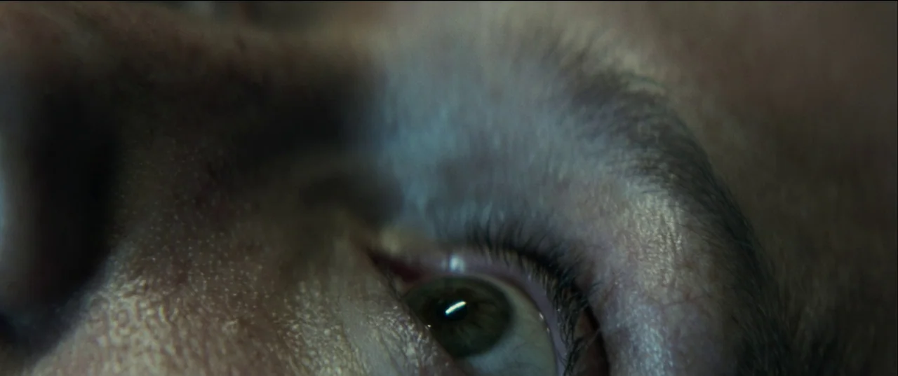Birth/Rebirth (2023) movie still: closeup — A close extreme view focuses on human skin and a single eye. The subject is partially illuminated while…