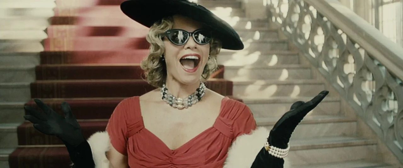 Enemy (2013) movie still: medium — A grand stone staircase features a red carpet runner and ornate wrought-iron railings. A woman in 1950s attire…