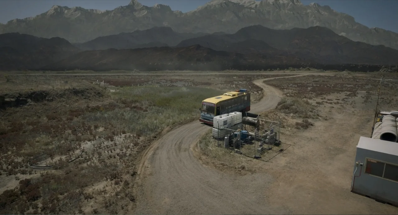 Ice Road: Vengeance (2025) movie still: wide — A dry desert landscape features rugged mountains in the distance and sparse scrub brush. A yellow bus…