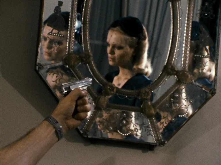 Making of: World On A Wire (1973) movie still: medium — A person holds a handgun directed at a highly ornate, antique-style wall mirror. Inside the…