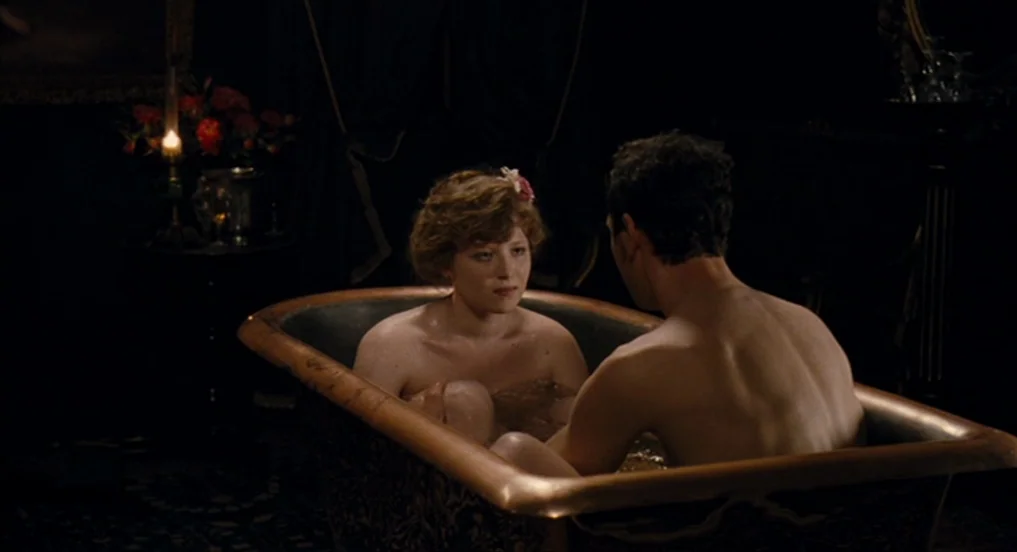 House of Tolerance (2011) movie still: medium — A dark, shadowed room contains a large copper bathtub filled with water. A woman with short hair and…