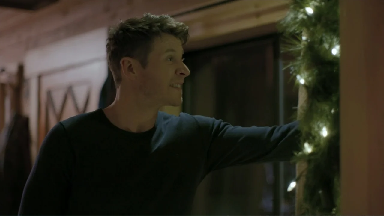 Alex & Emma (2003) movie still: medium — The interior of a wooden structure features a decorative green garland with white lights. A man in a dark…