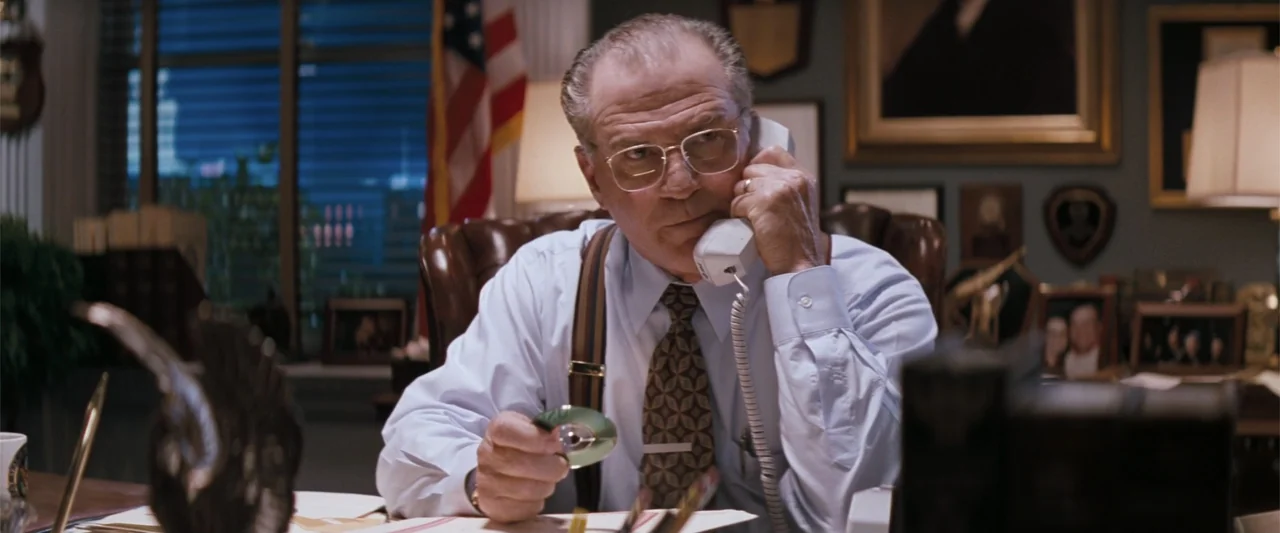 The Eraser (1977) movie still: medium — A wood-paneled office contains desk clutter, framed photos, and an American flag background. An older man…