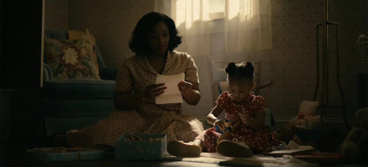 Devotion (2022) movie still: medium — A dimly lit room with patterned wallpaper and furniture illuminated by backlight from a window. A woman sits…