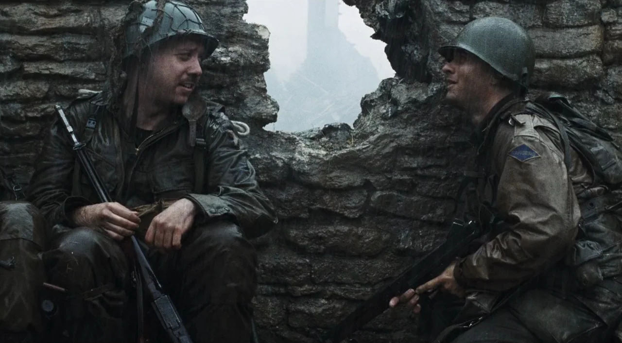 Saving Private Ryan (1998) movie still: medium — Two US soldiers wait in a rain-slicked position behind a ruined stone masonry wall. They discuss…