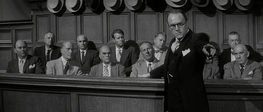 Compulsion (1959) movie still: medium — A wood-paneled courtroom interior features a row of men seated before a wooden partition. A man in a suit…