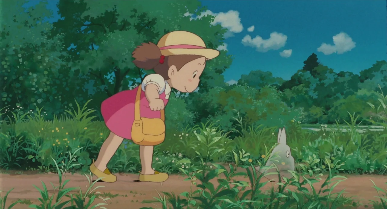 My Neighbour Totoro (1988) movie still: fullbody — A narrow dirt path winds through dense green bushes and trees under a clear sky. A young girl in…