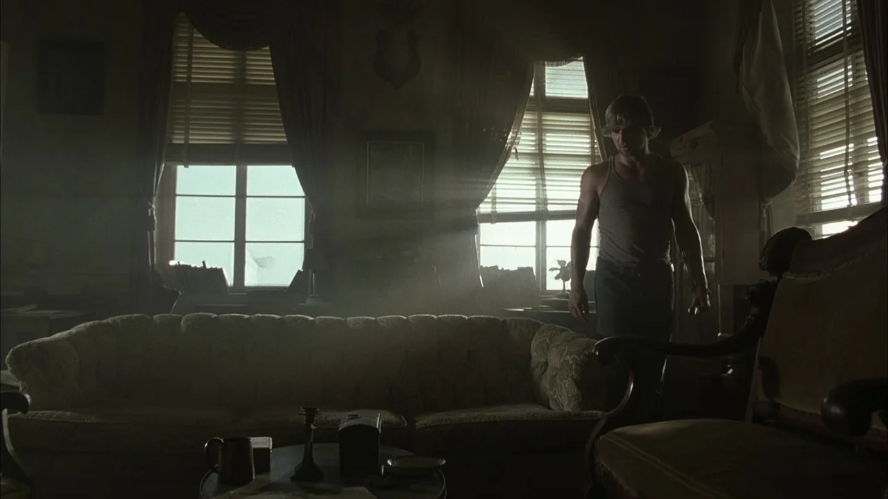 The Texas Chainsaw Massacre (2003) movie still: fullbody — A dimly lit room with antique furniture and light streaming through slatted window…