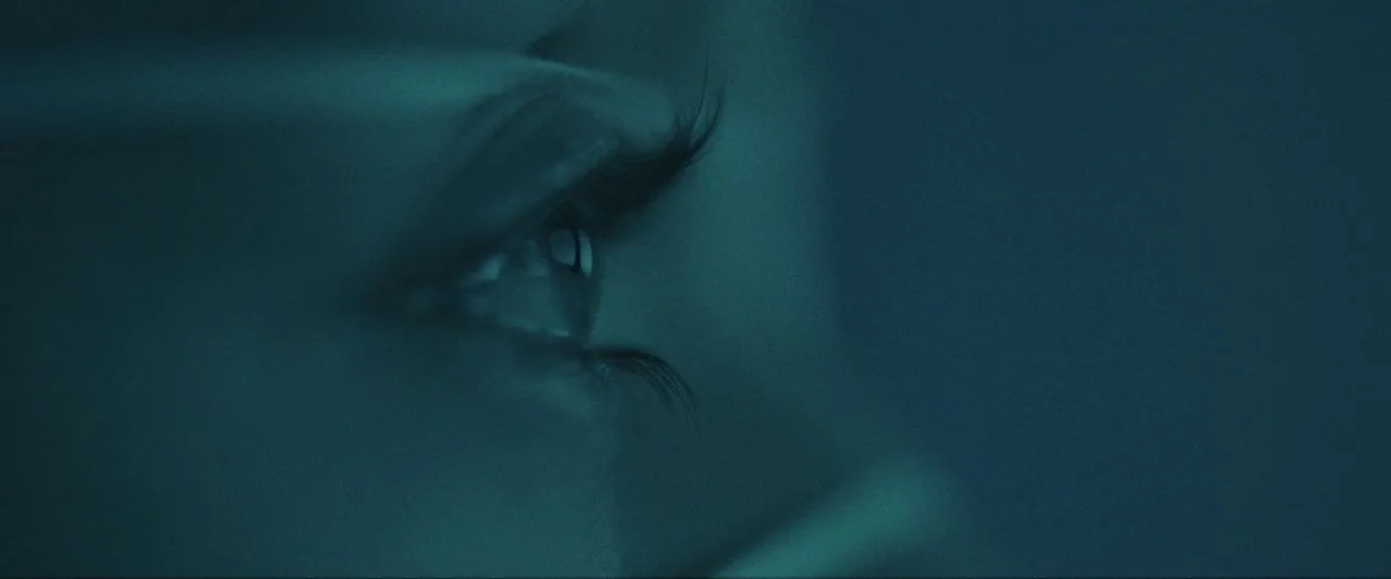 Come True (2020) movie still: closeup — An extremely close-up view of a single human eye in deep shadow. The person is looking toward the right of…