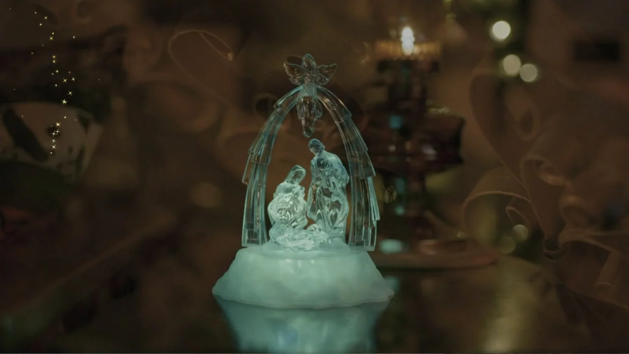 Alex & Emma (2003) movie still: closeup — A miniature glass nativity set sits on a dark reflective surface in a dim room. The central figurine glows…
