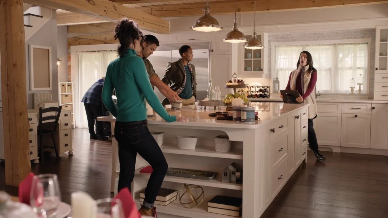 Designing Christmas (2022) movie still: wide — A bright contemporary home interior features white shaker cabinets and a large central island. Four…