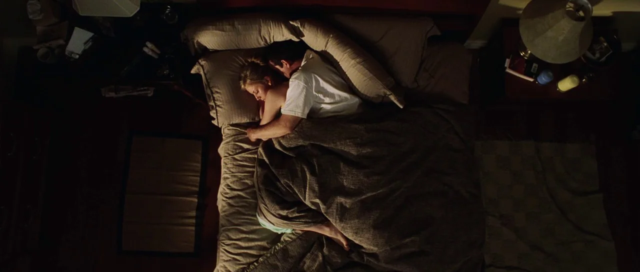 Dawn of the Dead (2004) movie still: wide — A top-down view shows a couple sleeping together in a large bed. The room features bedside tables with…