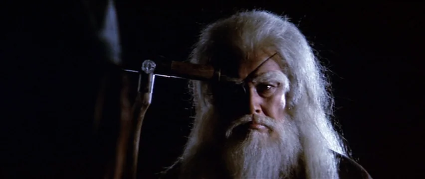 Lone Wolf and Cub: White Heaven in Hell (1974) movie still: closeup — A man with long white hair stands in darkness against a black background. He…