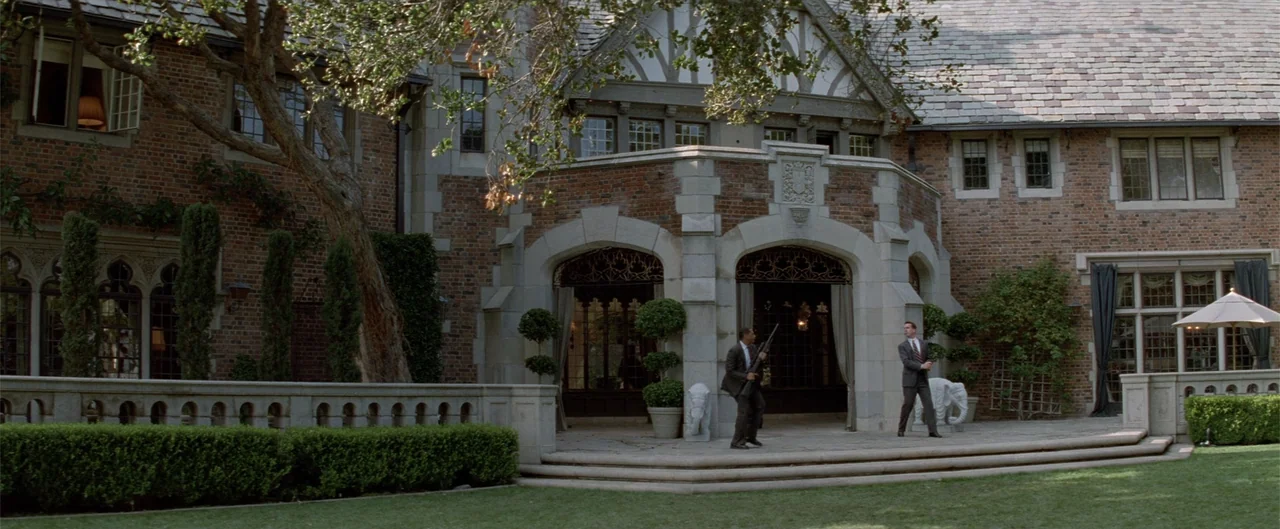 Rush Hour (1998) movie still: wide — A large brick manor with a prominent stone entryway and arched glass doors. Two men in business suits stand on…