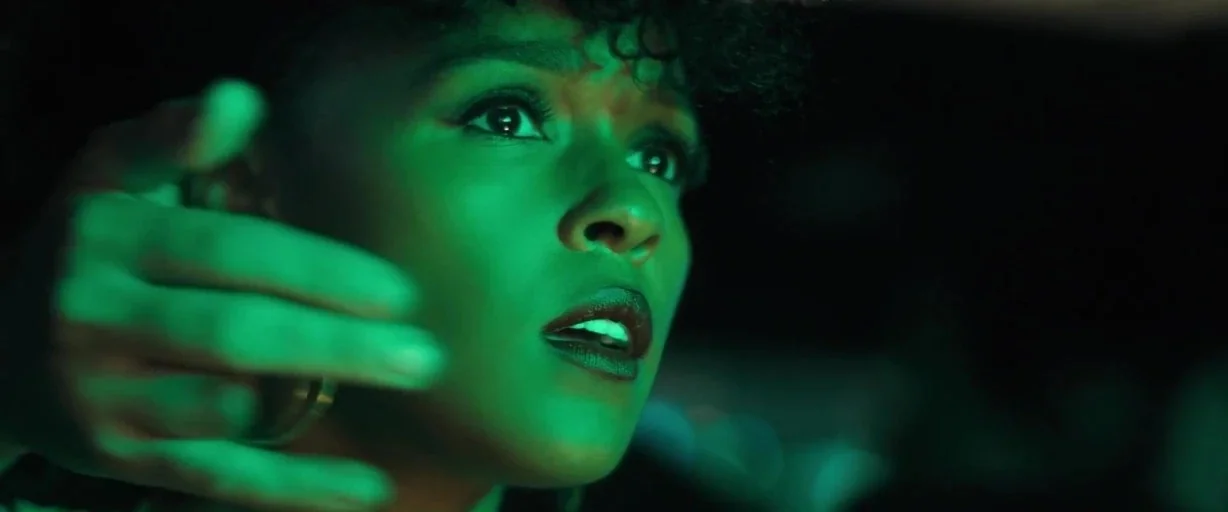 Antebellum (2020) movie still: closeup — The interior of a vehicle at night is bathed in a saturated green light. A woman with curly hair looks…