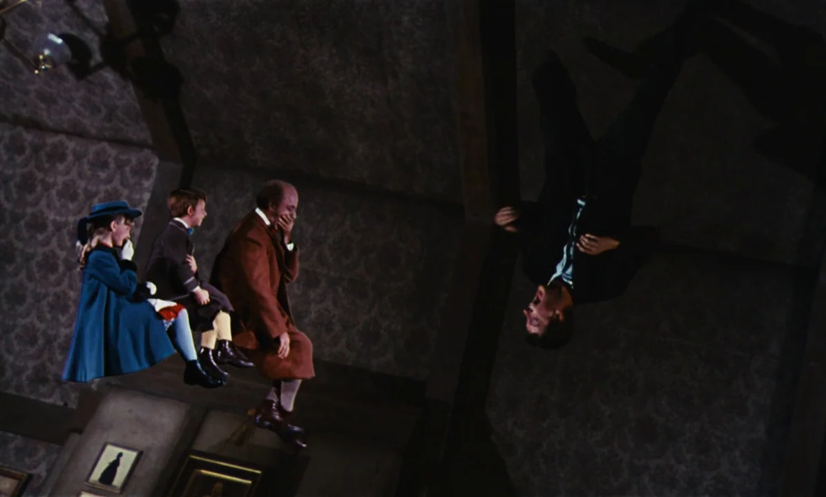 Mary Poppins (1964) movie still: fullbody — An interior living room with patterned wallpaper and dark wooden ceiling beams. Four people sit upright…