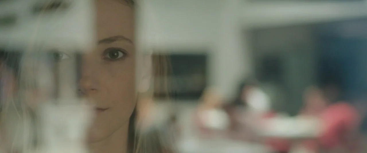 On Body and Soul (2017) movie still: closeup — A woman stands behind a glass pane in a brightly lit interior space. Her face is partially reflected…