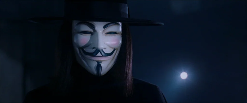 V for Vendetta (2006) movie still: closeup — A dark, indistinct space surrounds a figure wearing a stylized Guy Fawkes mask. The subject remains…