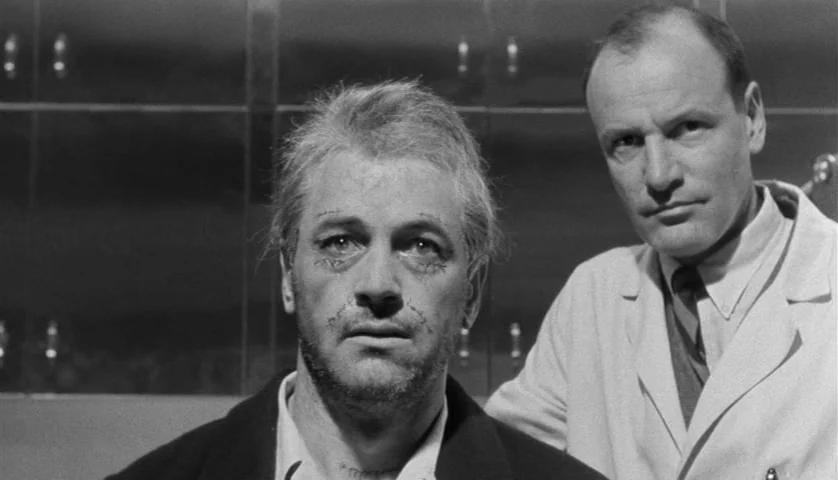 Seconds (1966) movie still: medium — A clinical laboratory features sterile metal wall cabinets in the background. A scarred man stands next to a…