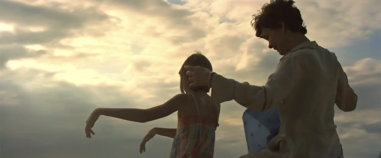 Dirty Little Secret (1998) movie still: medium — An open coastal area beneath a vast sky filled with clouds at golden hour. A woman stands beside a…