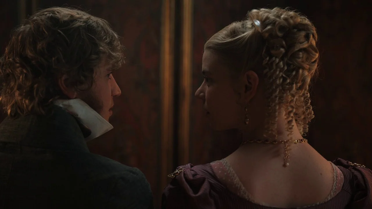 Emma. (2020) movie still: medium — Two individuals stand facing one another in a dark, dimly lit historical interior space. The man wears a cravat…