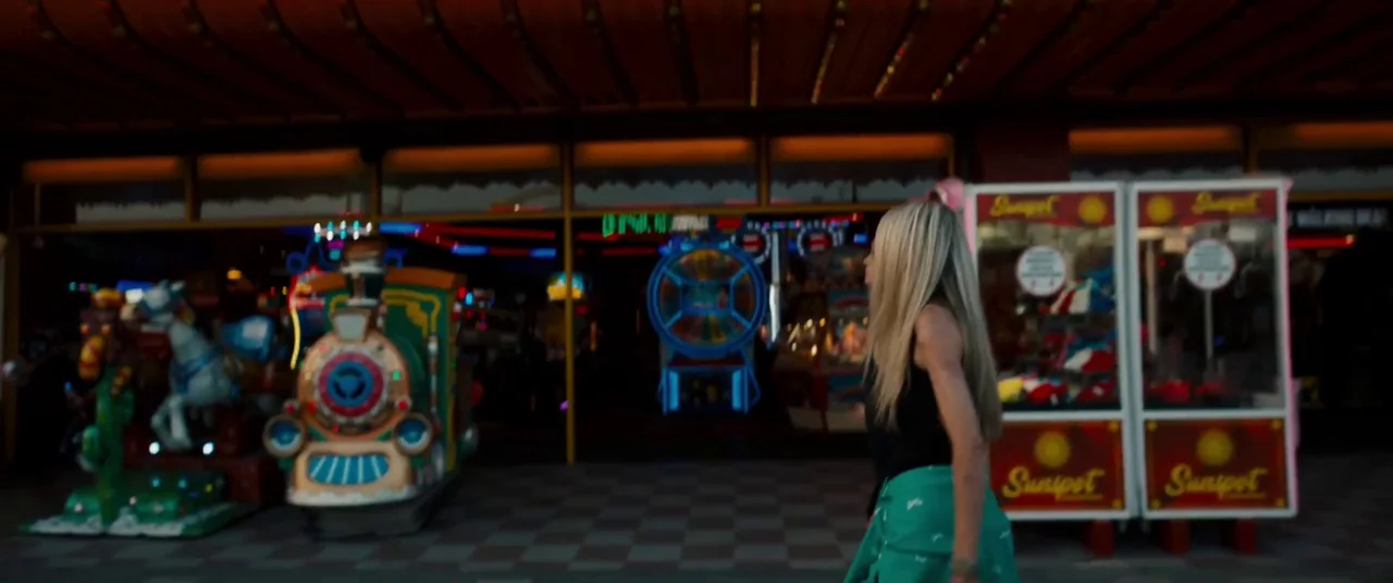 Silver Haze (2023) movie still: medium — An outdoor arcade entrance features colorful children's coin-operated rides and claw machines. A young…