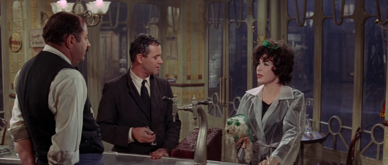 Irma La Douce (1963) movie still: medium — A classic bar interior with art nouveau style glass windows and warm lighting. A man stands at the…