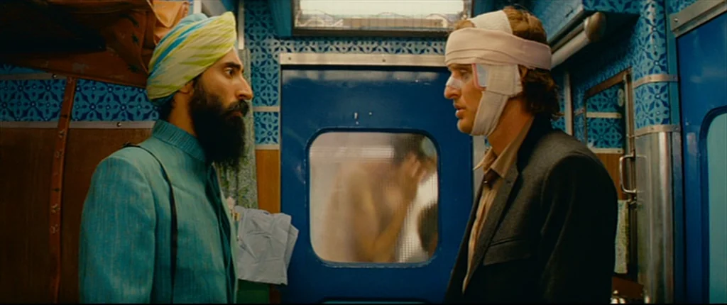 The Darjeeling Limited (2007) movie still: medium — A cramped train compartment features blue patterned walls and a rectangular sliding door window.…