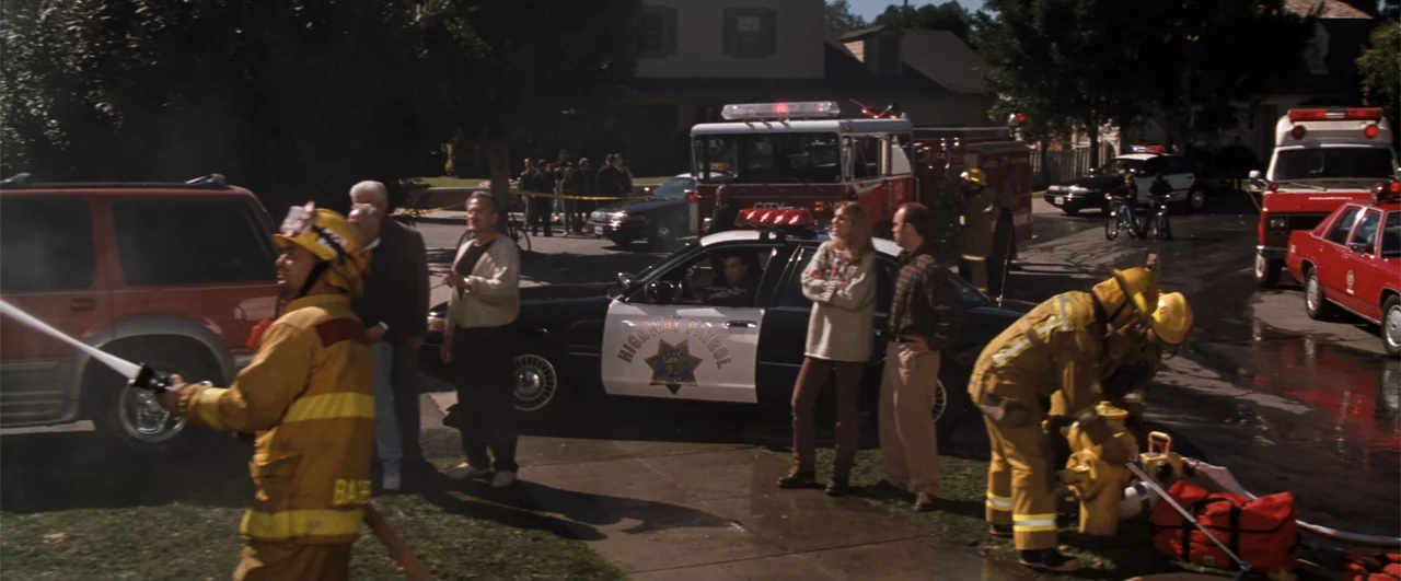 Lethal Weapon 4 (1998) movie still: wide — A suburban street scene features emergency vehicles parked near a residential home. Firefighters and…