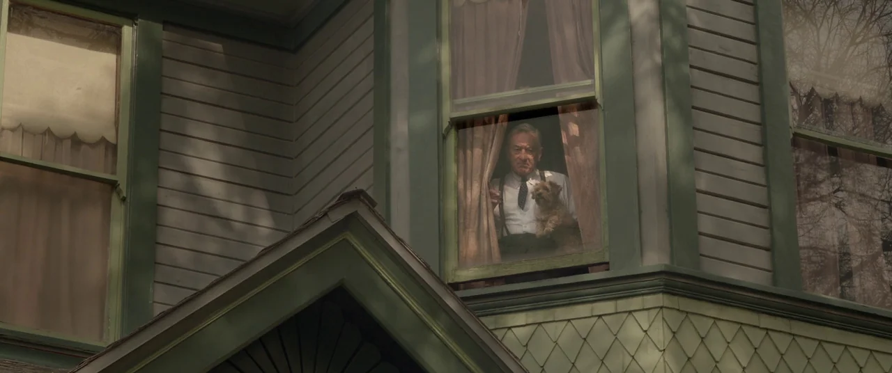 Amsterdam (2022) movie still: medium — An old wooden house with green trim features a large window on the upper level. An elderly man in formal…