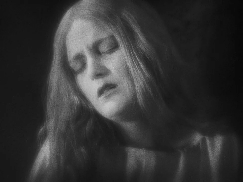 Faust (1926) movie still: closeup — A close-up shot focusing on a woman with closed eyes against a dark background. The lighting emphasizes the…