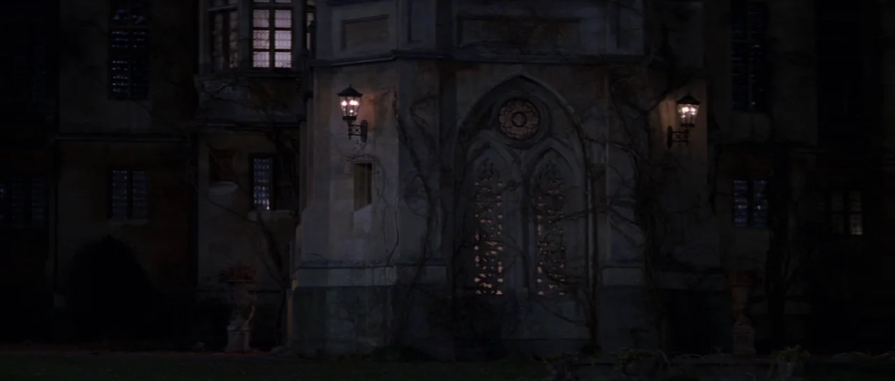The Haunting (1999) movie still: establishing — The exterior of an old stone manor features ornate gothic carvings and climbing vines. Two lit…