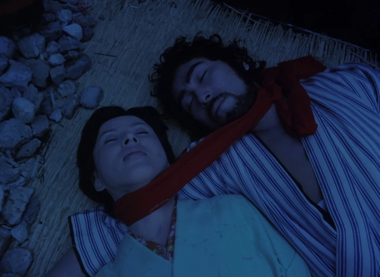 Pastoral To Die In The Country (1974) movie still: medium — A man and woman lie together on a woven straw mat under night moonlight. A long red…
