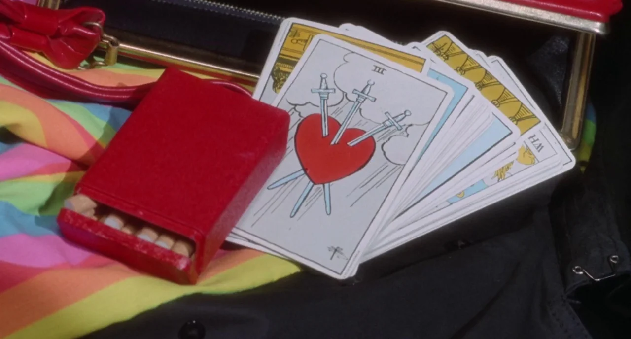 The Love Witch (2016) movie still: closeup — Inside a black handbag rests a pack of cigarettes and a fanned tarot deck. The top visible tarot card…