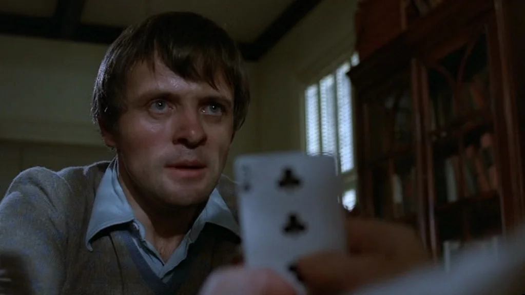 Magic (1978) movie still: closeup — A dimly lit room features dark wood furniture and a window with white shutters. A man holds a playing card in…