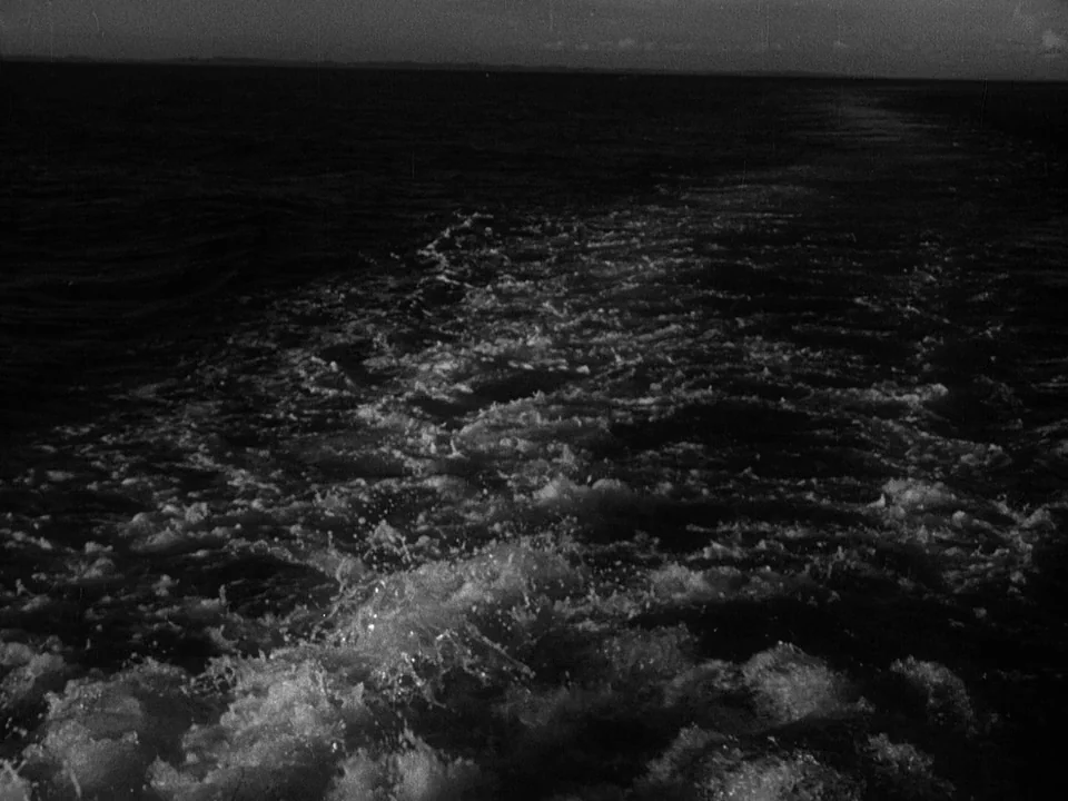Godzilla (1954) (1954) movie still: establishing — The open ocean at night reveals a turbulent white wake trailing from a boat. The dark water…