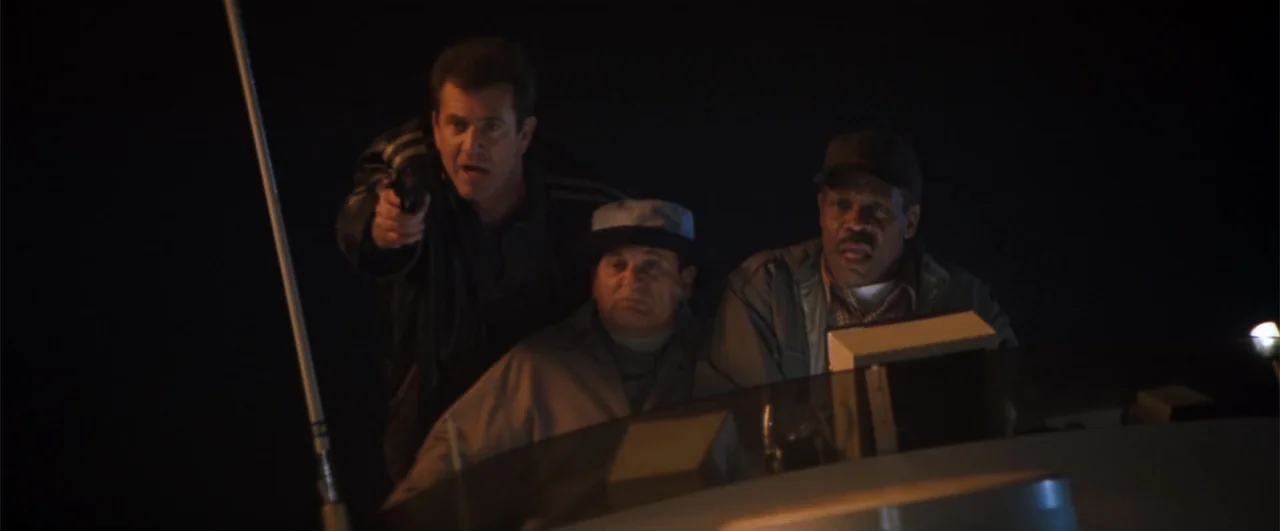 Lethal Weapon 4 (1998) movie still: medium — The deck of a boat is shrouded in darkness at night. Three men stand together while one holds a pistol.