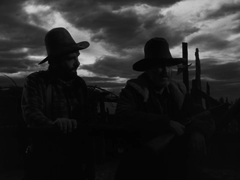 My Darling Clementine (1946) movie still: medium — Two men stand outdoors before a wooden rail fence under a dark cloudy sky. They are positioned in…