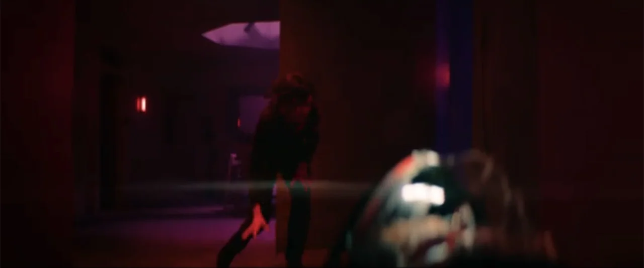 Ash (2025) movie still: medium — A dark, neon-lit corridor with deep shadows and magenta light spill. A person stands at the end of the hallway…