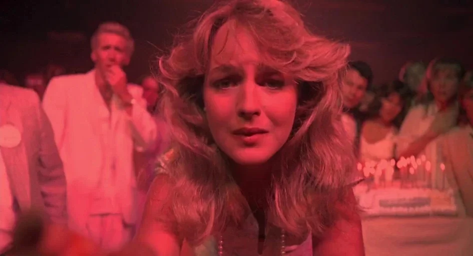 Peggy Sue Got Married (1986) movie still: closeup — A crowded reception hall is illuminated by a deep red light source. A young woman centers the…