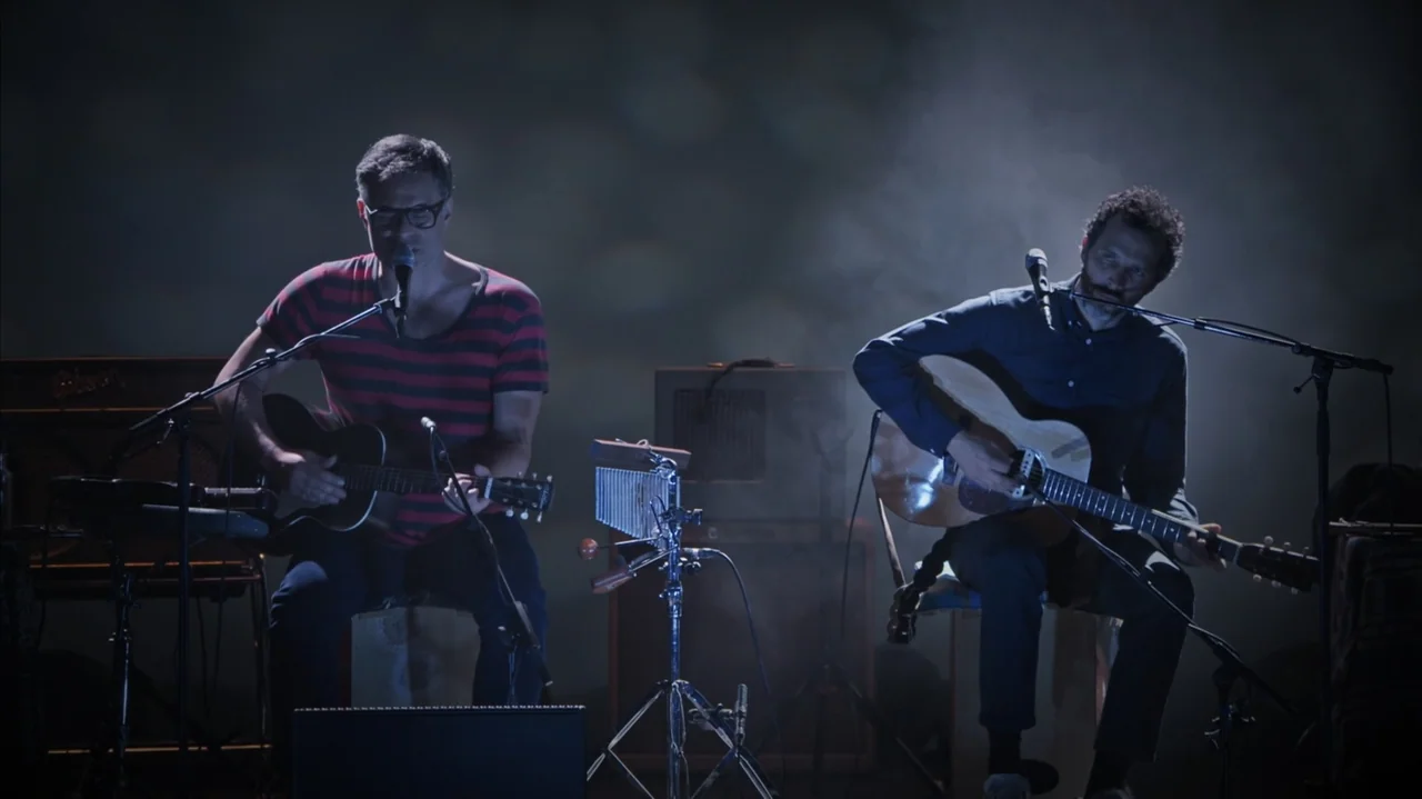 Flight of the Conchords: Live in London (2018) movie still: medium — A darkened music studio contains two performers sitting on stools with various…